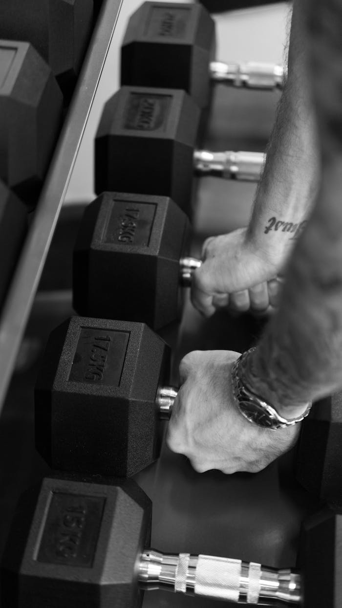 services-03 Black and white image of hands gripping dumbbells, showcasing fitness and strength training.